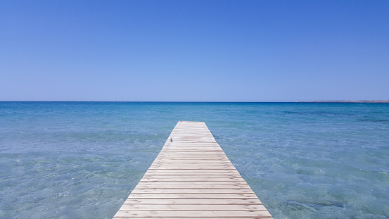 Wooden pier with blue sea and blue sky on background. Wooden bridge on the beach to the sea in the blue sky. Wooden bridge on the beach and blue sky in summer.