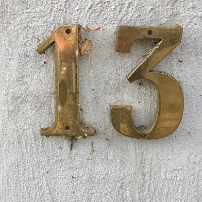 Street Number 13 in brass on white wall with dirt and spider web.