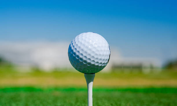 istock Golf ball on tee on golf course over a blurred green field at the sunset. Golf ball on tee over a blurred green field. 1267996840