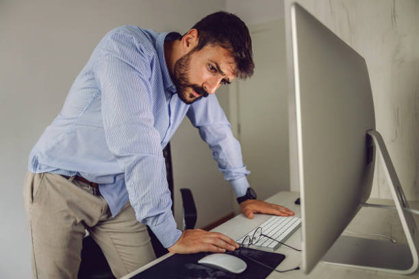 istock Young attractive bearded businessman standing in his office, leaning on table and thinking about solution for problem on the project. 1268003010