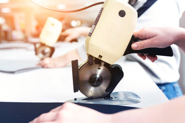 istock Female worker uses electric cutting fabric machine. 1268004936