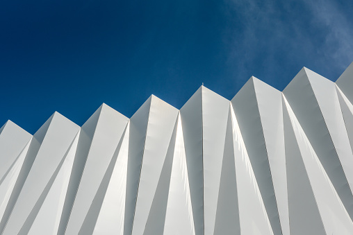 Abstract background with a white triangular pattern on a clear sky background. Siding on the wall of a public parking lot to provide shade and passage of the breeze.