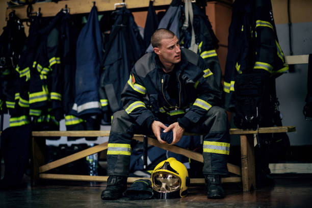 istock Young attractive fireman in protective uniform sitting in fire station and waiting for other firemen. He is prepared for action. 1268016916