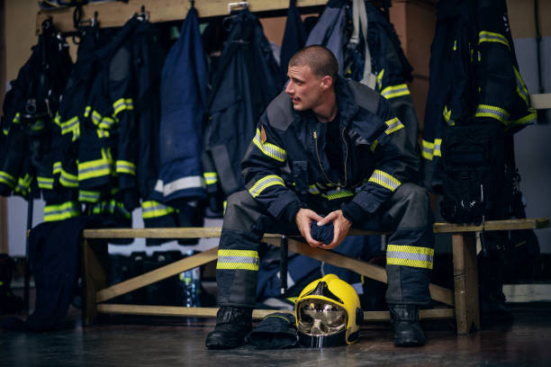 istock Young attractive fireman in protective uniform sitting in fire station and waiting for other firemen. He is prepared for action. 1268016997