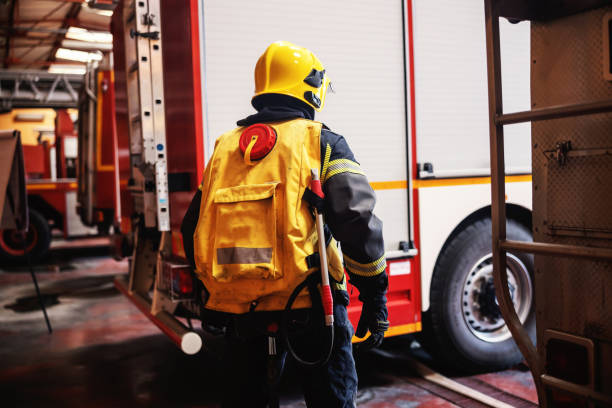 istock Rear view of brave firefighter in full protective uniform with equipment standing in fire station and preparing for action. 1268017016