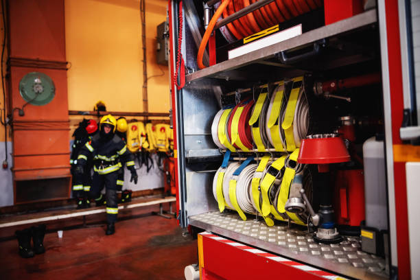 Opened fire truck with hoses. In background is firefighter preparing for action.