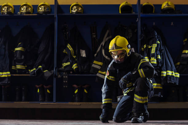 istock Brave young firefighter in protective uniform with helmet on head kneeling in fire station prepared for action. 1268017870