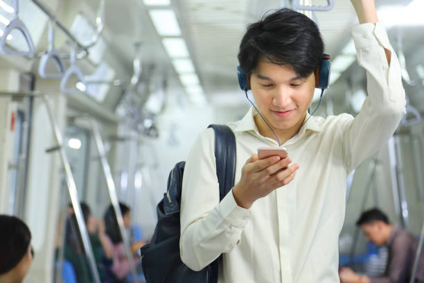 A lifestyle of young Asian man using cellphone with headset while taking the subway train to work at the rush hour morning A lifestyle of young Asian man using cellphone with headset while taking the subway train to work at the rush hour morning with copy space asian man headphones stock pictures, royalty-free photos & images