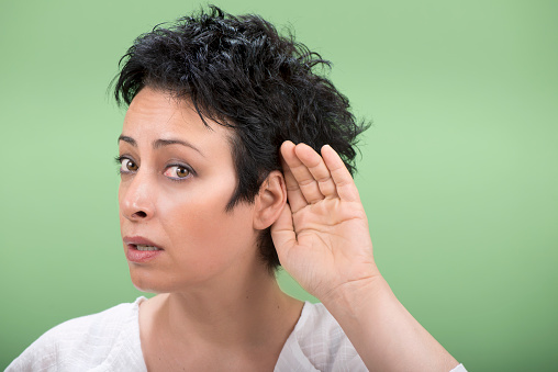 Adult woman can't hear something, puts hand behind her ear.
