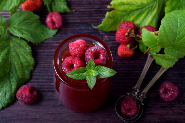 raspberry jam in glass jar topped with berries and mint - raspberry table wood autumn imagens e fotografias de stock