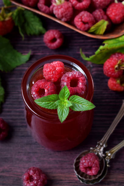 raspberry jam in glass jar topped with berries and mint - raspberry table wood autumn imagens e fotografias de stock