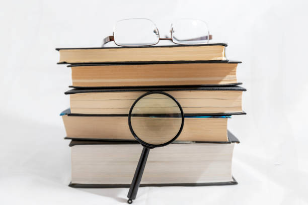 istock stack or bunch of Books with spectacles and the magnifying glass lens on white backgound 1268024419