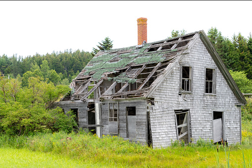 An old abandoned house in poor condition. Much of the roof is missing, and there is no glass in the windows. It looks like it will fall over soon.