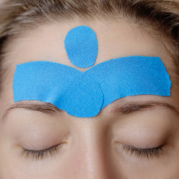 hermosa mujer con cintas de kinesio verticales en la frente contra las arrugas, procedimiento de belleza de estiramiento facial. - kinesio fotografías e imágenes de stock