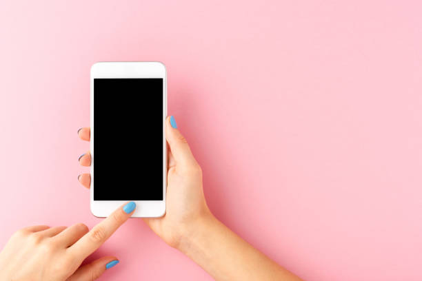 istock Woman’s hand with blue nails holding mobile phone with empty screen on pink background. Top view 1268028868