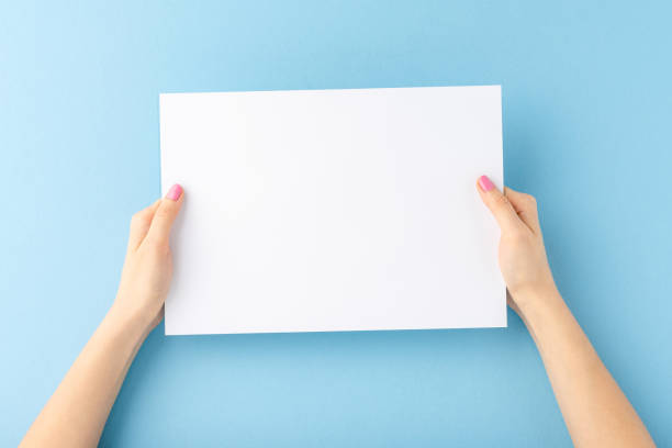 istock Young female hands showing empty white paper sheet on blue background. Mockup 1268028915