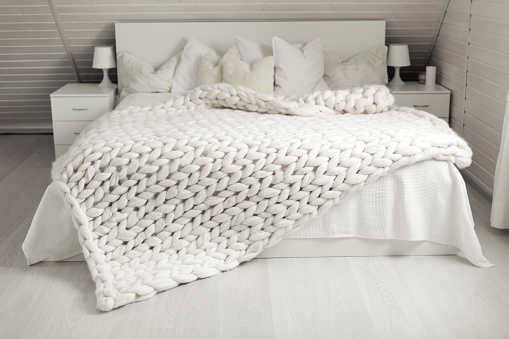 Cozy white scandinavian bedroom interior. Beautiful merino woolen plaid decorated bed and floor, super chunky yarn knitted blanket, nobody