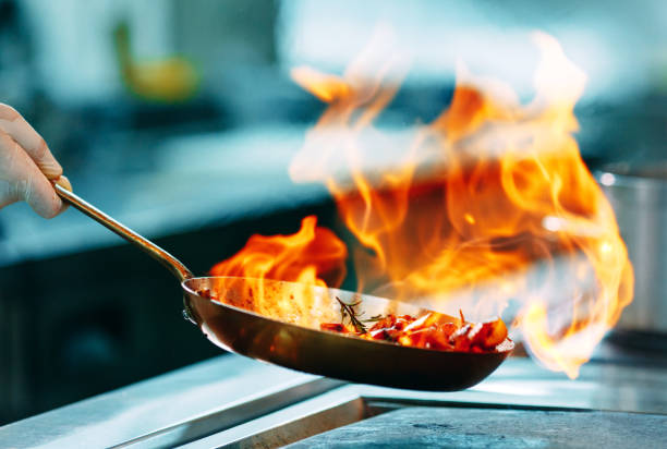 モダンなキッチン。料理人はレストランやホテルのキッチンでストーブの上で食事を準備します。台所の火事。 - flambe ストックフォトと画像