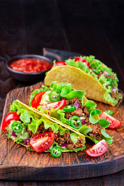 istock Taco shells with lettuce, ground beef meat,  mashed avocado, tomato, red onion and jalapeno pepper, on wooden board, vertical, copy space 1268032758