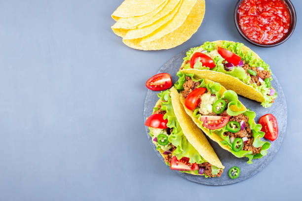 istock Taco shells on stone plate, with lettuce, ground beef meat,  mashed avocado, tomato, red onion and jalapeno pepper, horizontal, top view, copy space 1268032760