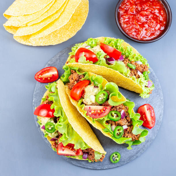 istock Taco shells with lettuce, ground beef meat,  mashed avocado, tomato, red onion and jalapeno pepper, on stone plate, square format, top view 1268032761
