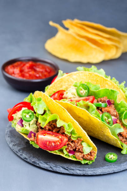 istock Taco shells on stone plate, with lettuce, ground beef meat,  mashed avocado, tomato, red onion and jalapeno pepper, vertical, closeup 1268032767