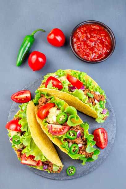 istock Taco shells on stone plate, with lettuce, ground beef meat,  mashed avocado, tomato, red onion and jalapeno pepper, vertical, top view 1268032773