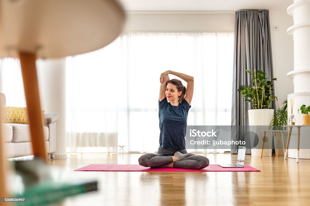 Building a stronger core Attractive young woman doing yoga stretching yoga online at home. Self-isolation is beneficial, entertainment and education on the Internet. Healthy lifestyle concept. Yoga Stock Photo