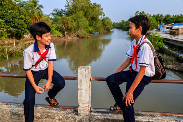 istock Two Vietnamese schoolboys sitting on a bridge, Mekong River Delta, Vietnam 1268039562