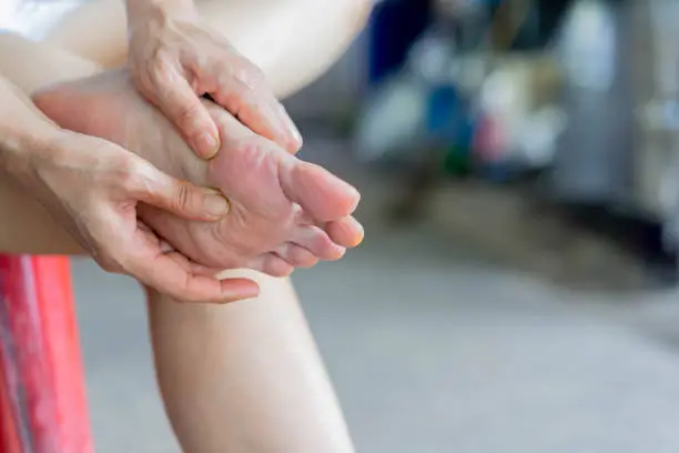 close up adult woman hand holding foot to massing after feeling pain from gout symptoms for healthy life concept
