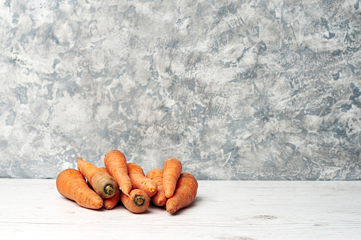 Heap of fresh natural raw carrots on a light wooden table and gray background