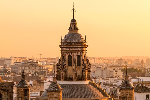 A close-up golden sunset view of the dome and bell tower at the top of the 16th-century Renaissance style Iglesia de la Anunciación - The Annunciation Church in Seville, Andalusia, Spain.