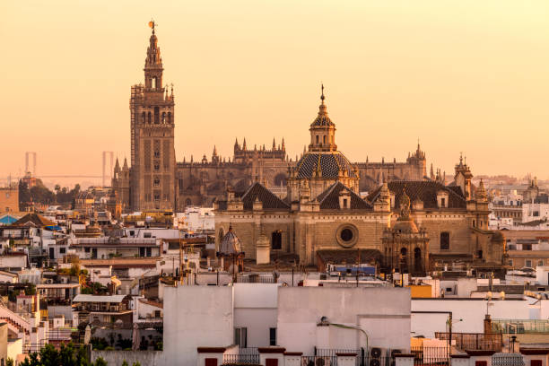 sonnenuntergang sevilla - ein panorama-goldenen sonnenuntergang blick auf la giralda turm und dach der kathedrale von sevilla steigt hinter der hohen kuppel der kirche des göttlichen erlöser. sevilla, andalusien, spanien. - seville sevilla santa cruz city stock-fotos und bilder