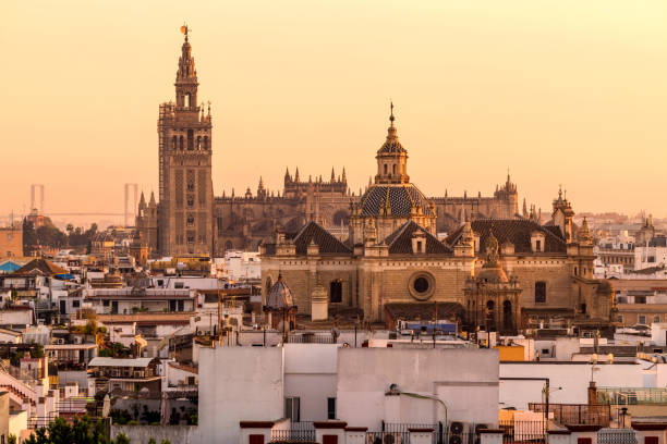 sunset seville - a panoramic golden sunset view of la giralda tower and rooftop of seville cathedral rising behind soaring dome of the church of the divine saviour. seville, andalusia, spain. - architecture europe seville spain imagens e fotografias de stock