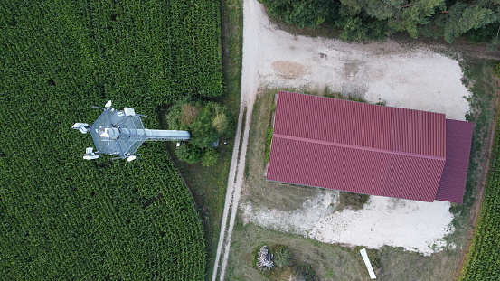 Ansbach, Germany / Bavaria - August 22, 2020: Wide Area Network (WAN) 3G 4G 5G LTE mobile radio broadband transceiver communications tower with, corn field, building , and view from above.