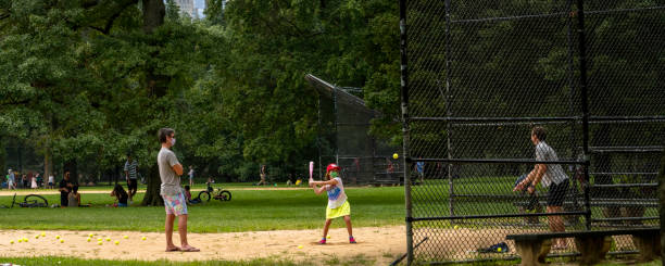 Young Girl in Mask Practices Baseball in Central Park During Coronavirus New York, NY, USA - August 23, 2020: A young girl practices her swing at one of Central Park's baseball fields on the Great Lawn. baseball cage stock pictures, royalty-free photos & images