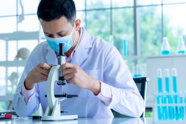 istock medical scientist wearing protective surgical mask and lab gown using microscope in clinical laboratory 1268070925