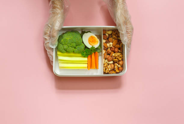 Hands in protective gloves with a healthy lunch in a box. Horizontal top view on a pink background stock photo