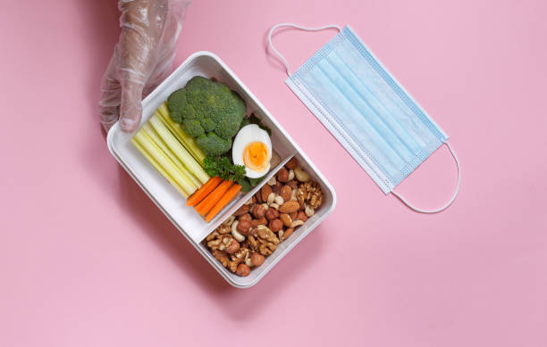 Hands in protective gloves with a useful lunch in a box and a protective mask. Horizontal top view on a pink background stock photo