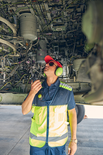 Front view of an aircraft maintenance technician in uniform examining the underside of the fuselage