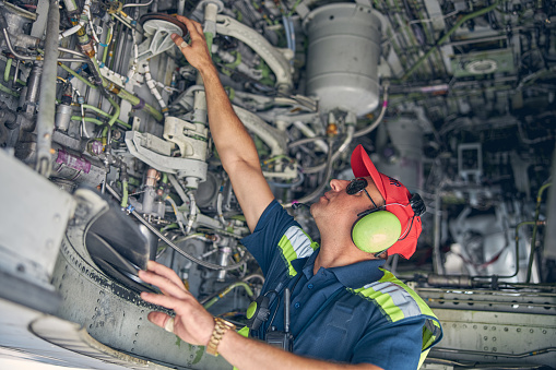 Side view of a professional aviation mechanic performing a routine inspection of the aircraft bottom