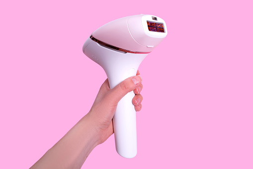 The girl holds a photoepilator in her hand. A device for removing unwanted hair isolated on pink.