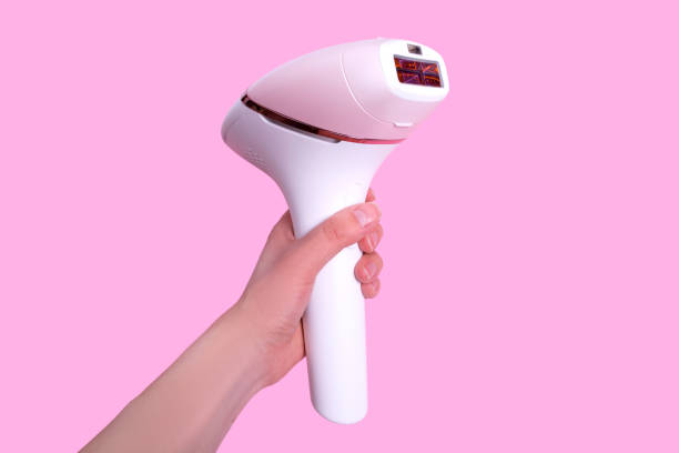 the girl holds a photoepilator in her hand. a device for removing unwanted hair isolated on pink. - beauty spa flash imagens e fotografias de stock