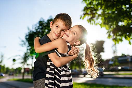 Beautiful little boy and girl are hugging outdoors on a sunset. Copy space.