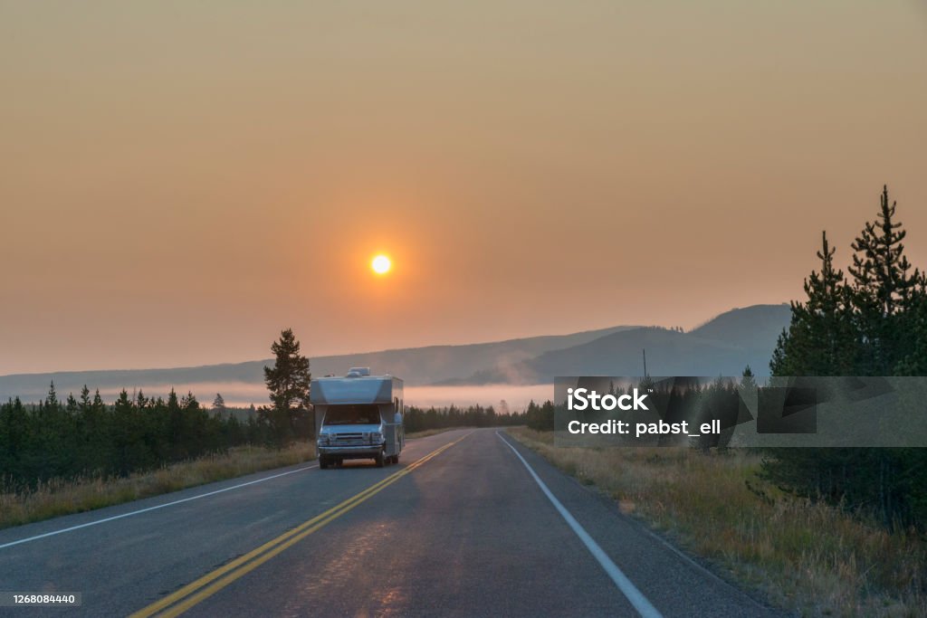 RV motorhome on roadtrip with sunrise in Yellowstone RV driving on the highway in yellowstone national park. Sunrise on the background on a smog smoky day. Idaho Stock Photo