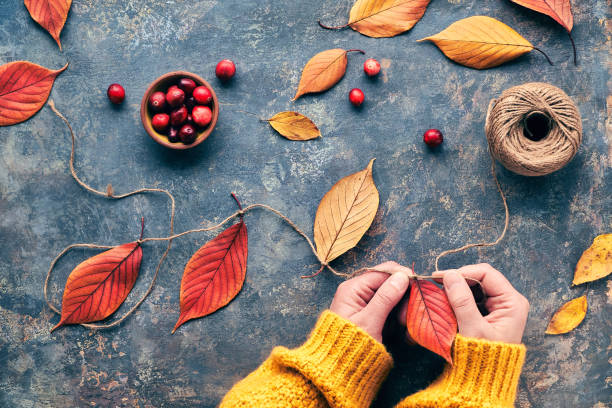 Fall decorations made from natural materials. Making garland with hemp cord and vibrant red Autumn leaves.