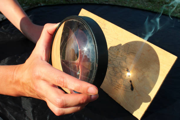 太陽光は、虫眼鏡を通過した木材を燃やす - magnifying glass lens holding europe ストックフォトと画像
