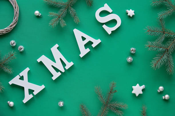 istock Creative Christmas flat lay with large white letters Xmas on green textile background. Geometric design with frosted Xmas tree twigs and toys. 1268109706