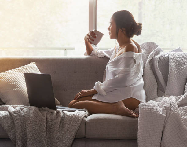istock Beautiful young woman using Laptop While Sitting On Sofa window on luxury apartment. 1268109777