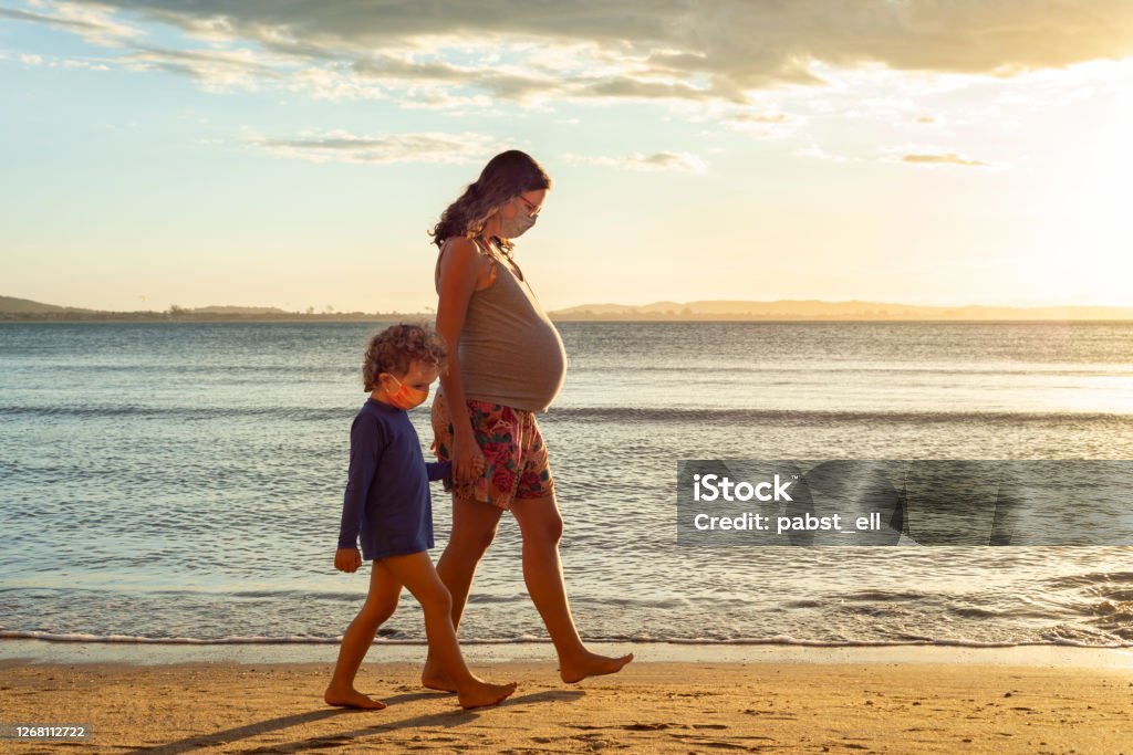 Pregnant mother walking hand in hand with son Pregnant mother exercising at the beach, holding her toddler's son hand by the sea, during sunset. Pregnant Stock Photo